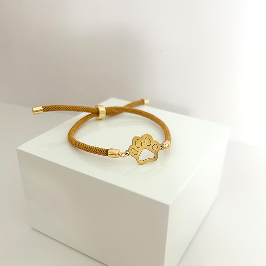 Adjustable pet paw bracelet with gold-tone paw charm and camel braided cord for dog lovers.