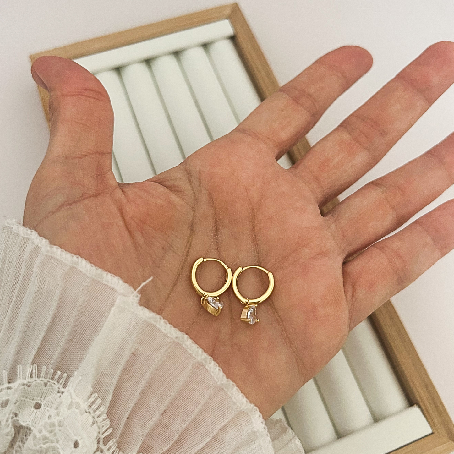 Pair of gold hoop earrings with heart crystal charm held in open palm