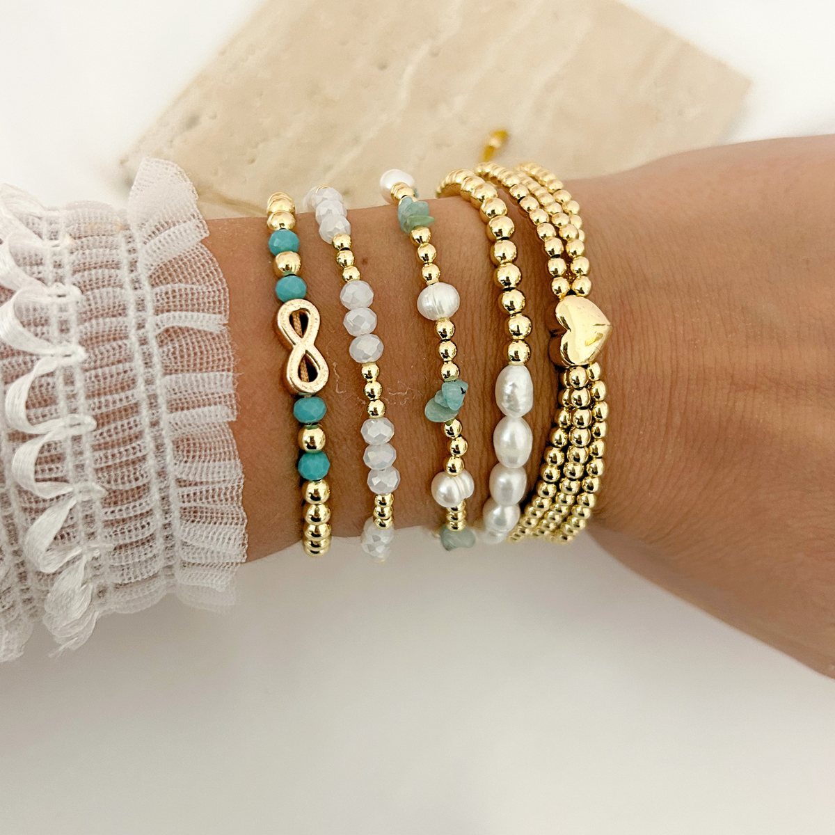 Layered gold bracelets featuring turquoise beads, freshwater pearls, an infinity charm, and a polished heart.
