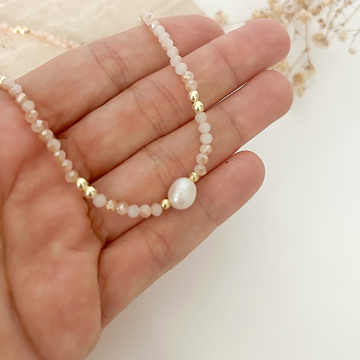 Close-up of a dainty blush pink beaded necklace with faceted beads, gold-tone details, and a luminous freshwater pearl centerpiece.