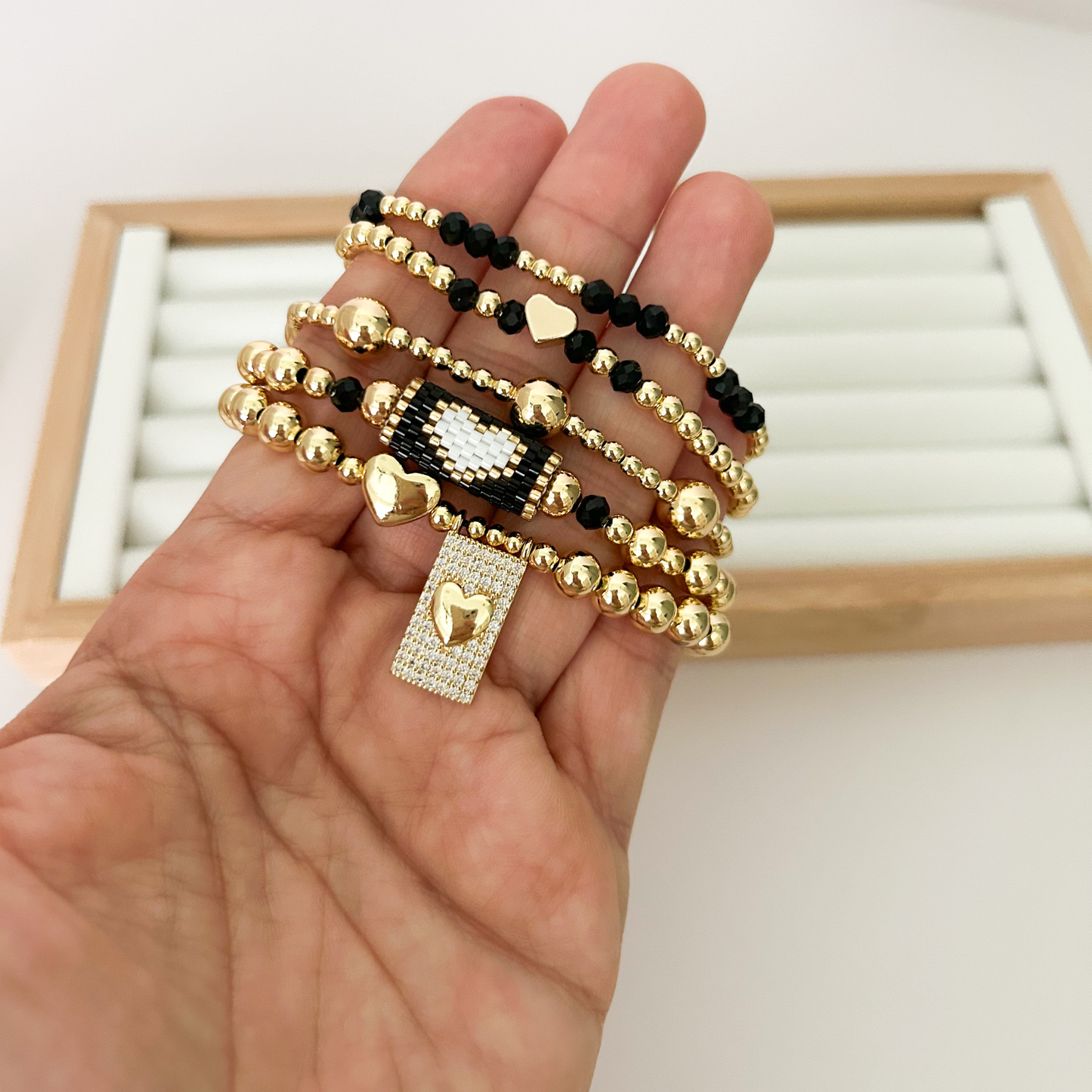 Five black and gold bracelets with miyuki accent and heart charm held in hand