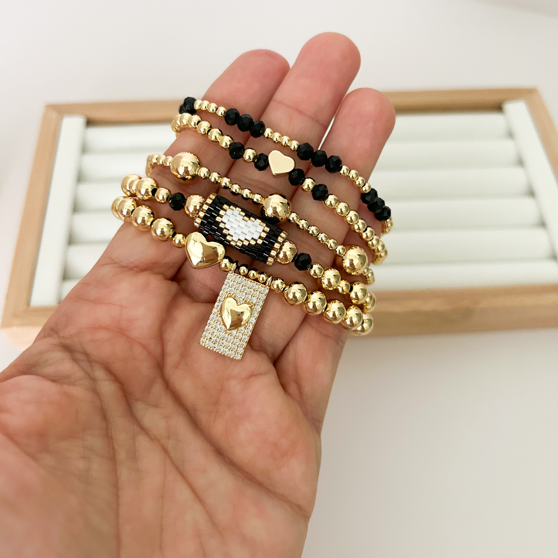 Five black and gold bracelets with miyuki accent and heart charm held in hand