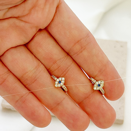 Small gold evil eye hoop earrings displayed in hand, featuring clear crystals and blue center stones.
