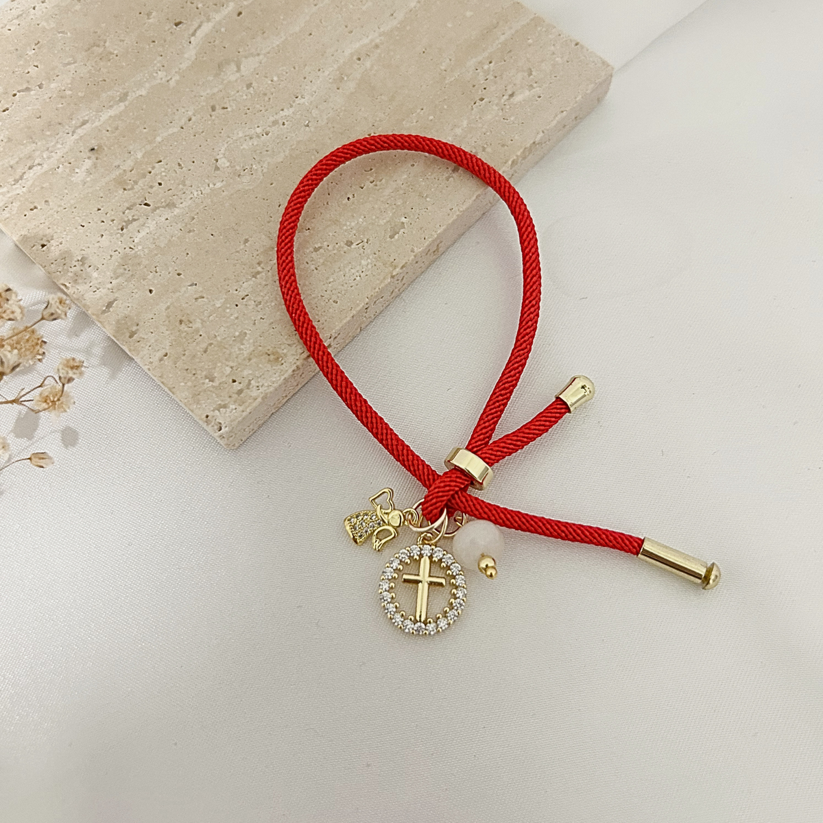 Red charm bracelet with gold cross and angel charms on a stone tray