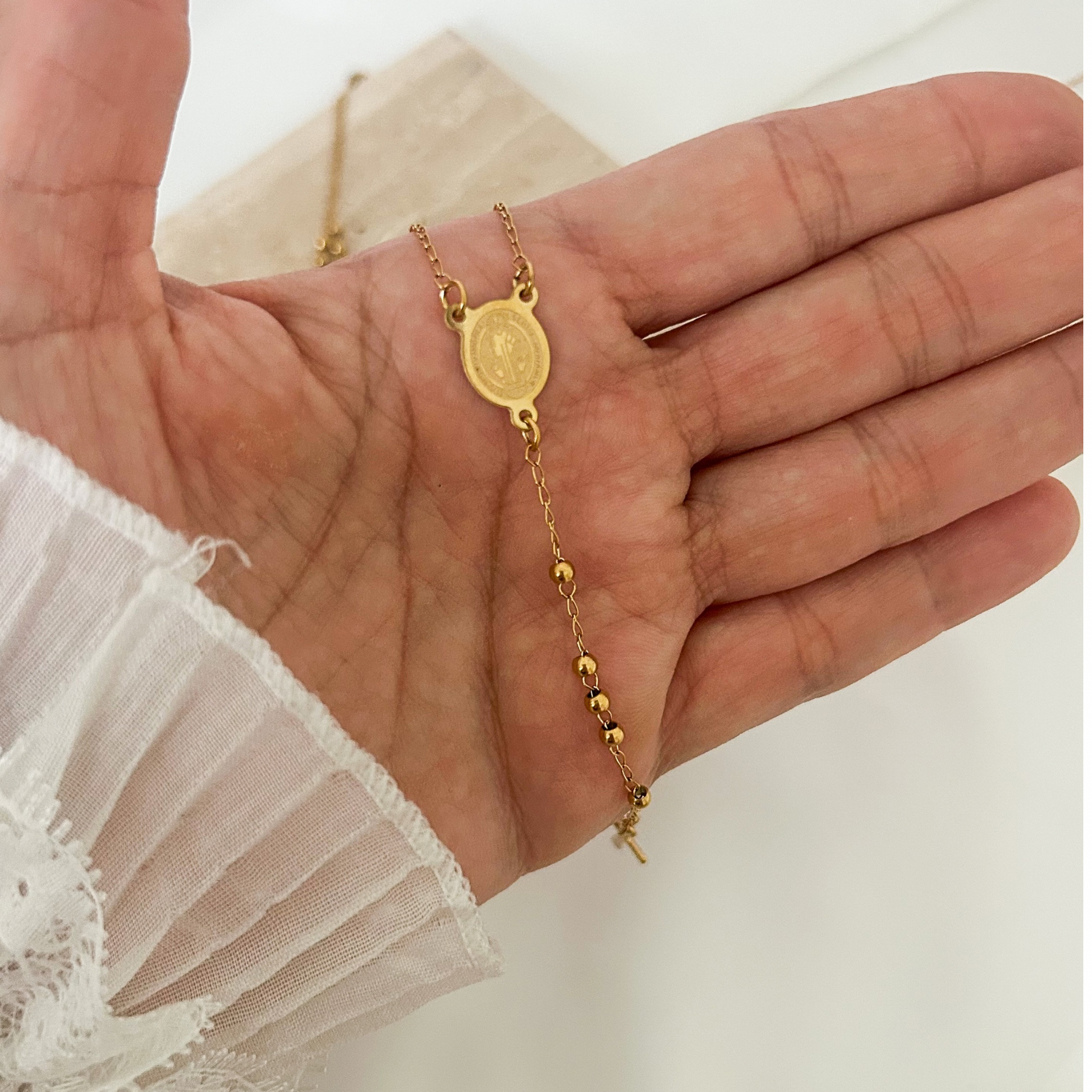 Close-up of a minimalist gold necklace with a Saint Benedict medallion, delicate bead accents, and a suspended cross charm, symbolizing faith, protection, and devotion.
