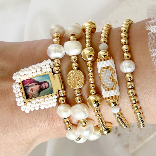 Multiple beaded bracelets with gold and pearl accents on a wrist against a white background