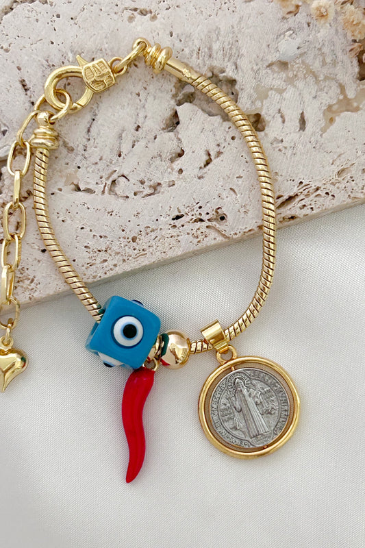 Gold bracelet with blue eye, red chili pepper, and coin charm on a textured surface