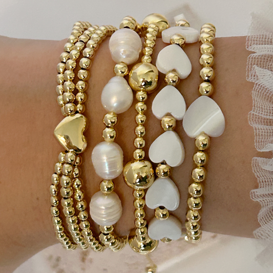 Stack of gold and pearl beaded bracelets on a wrist with a white lace background