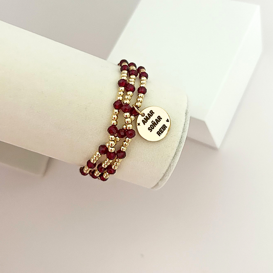 Elegant layered bracelet with deep burgundy beads and a gold-tone inspirational charm, designed for everyday wear.