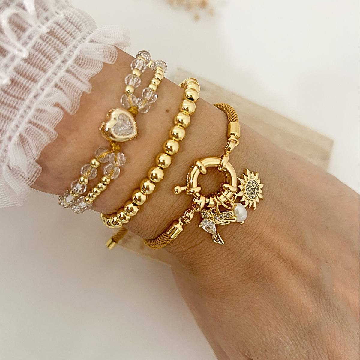 Stacked gold bracelet set with crystal heart, gold bead, and sun hummingbird charm bracelets