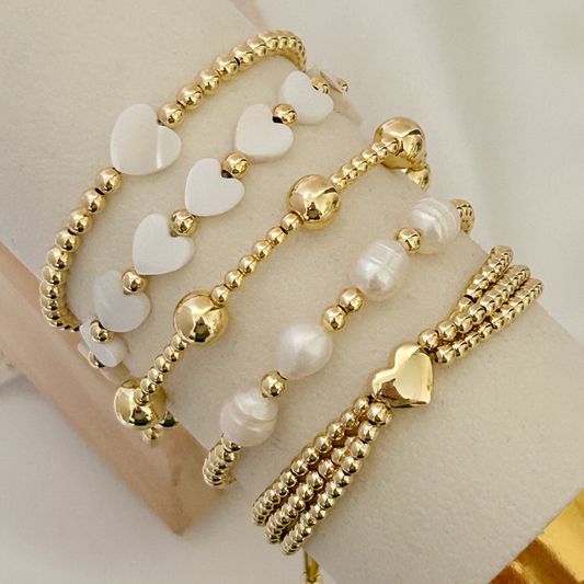 Gold and white beaded bracelets on a mannequin wrist with a plain background