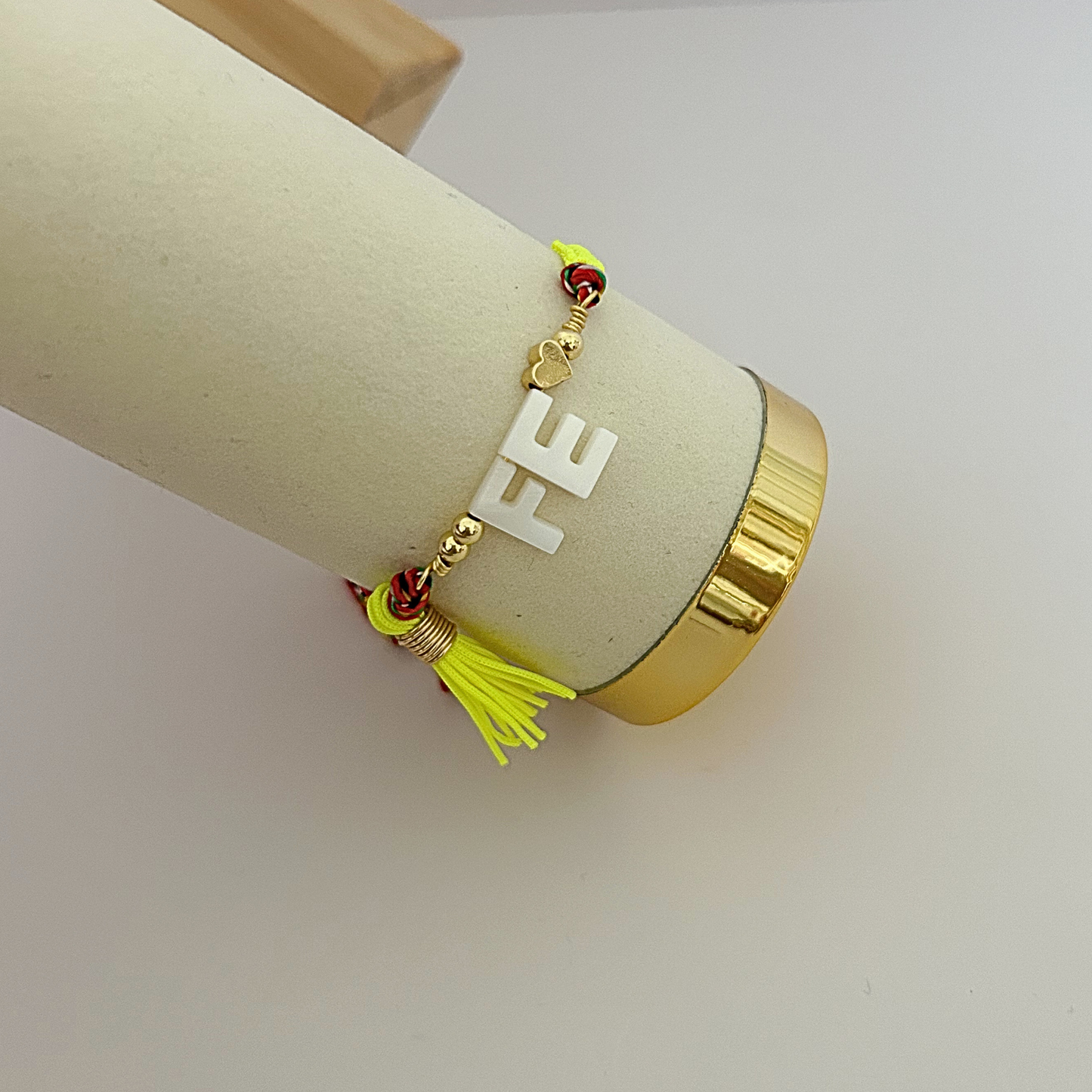 Neon yellow tassel bracelet with white “FE” charm and colorful braided cord details for women.