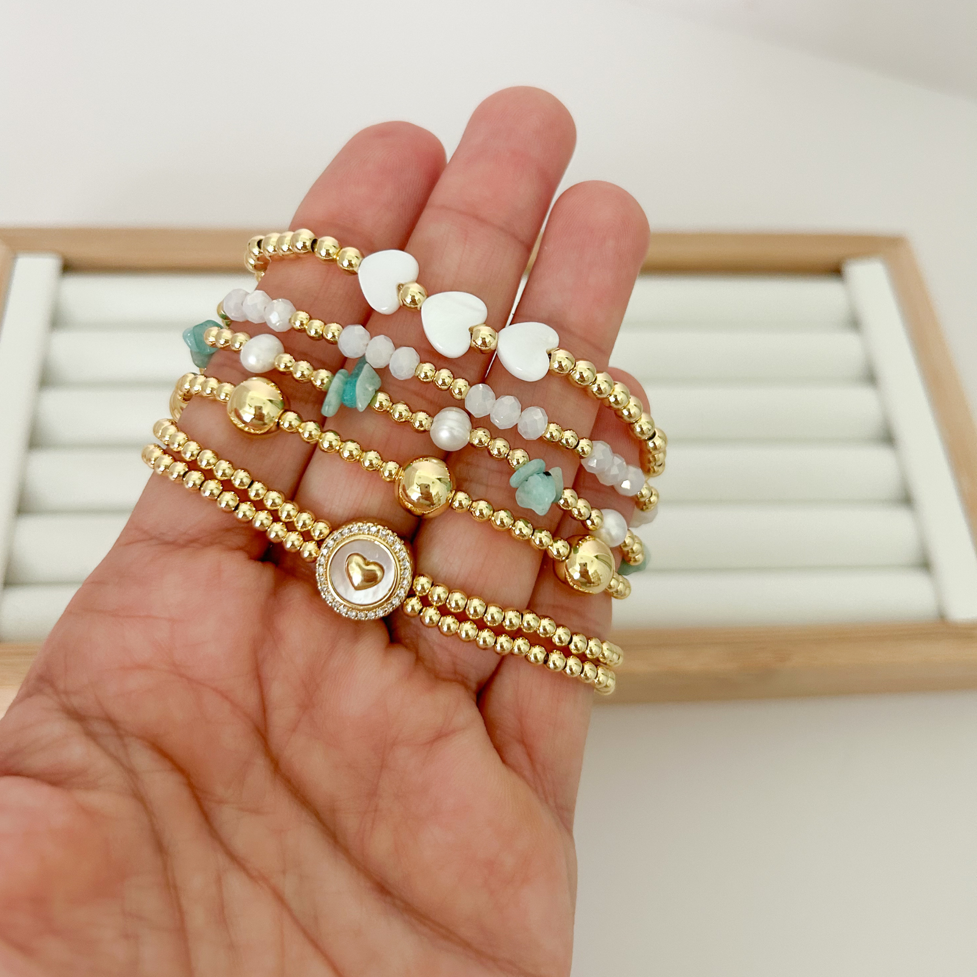 Five gold bracelets with green stones and pavé heart medallion held in hand