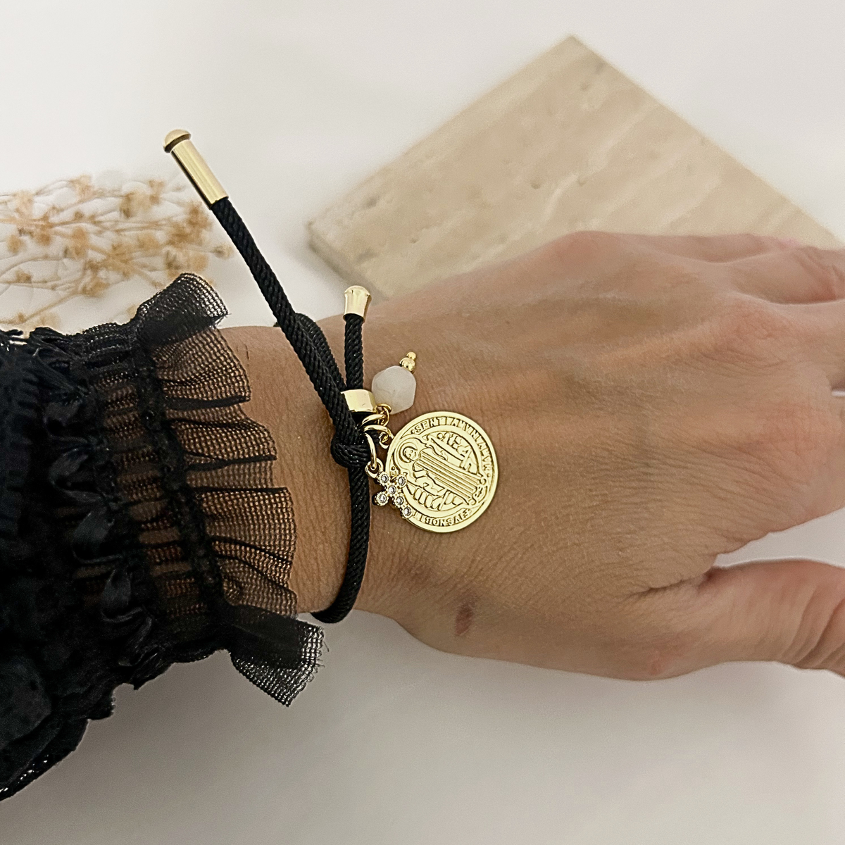 Black adjustable bracelet with Saint Benedict medal, zirconia cross, and white bead worn on the wrist