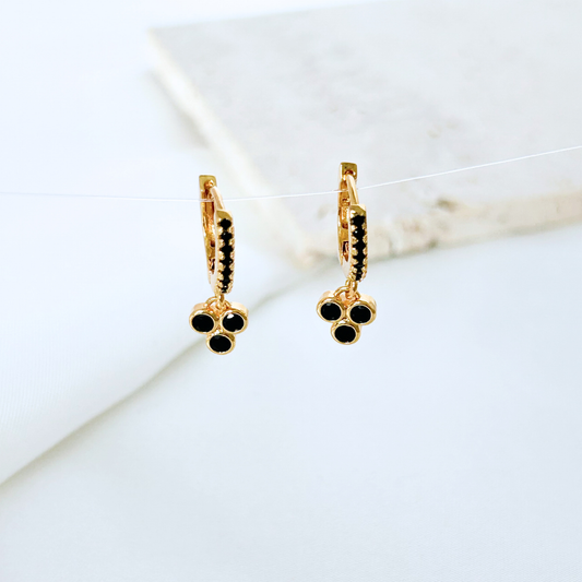 Gold hoop earrings with black gemstones on a marble surface