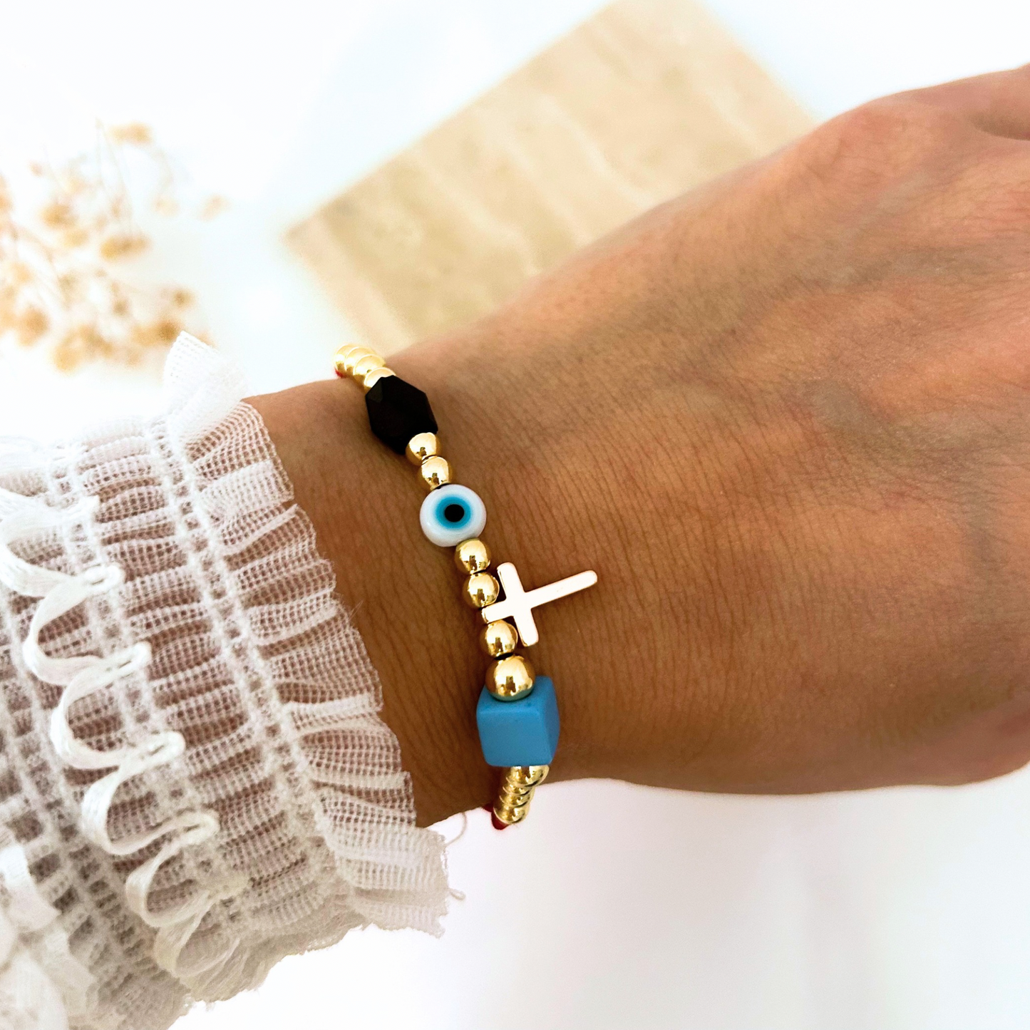 Adjustable red cord bracelet featuring gold-tone beads, a gold cross charm, a blue evil eye bead, and black and sky-blue accent beads. A meaningful everyday accessory that combines faith, protection, and modern style.