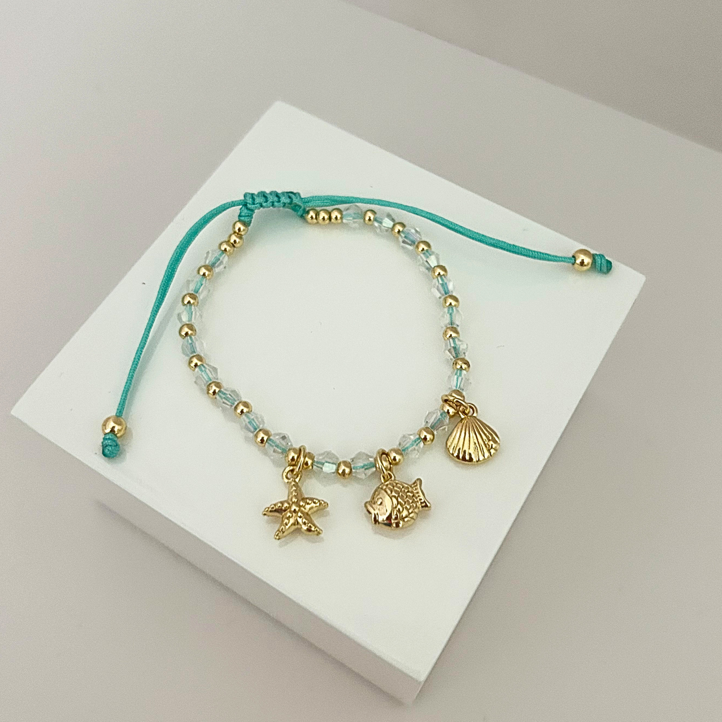 Adjustable beach-inspired bracelet featuring crystal beads, gold-tone accents, and starfish, fish, and seashell charms.