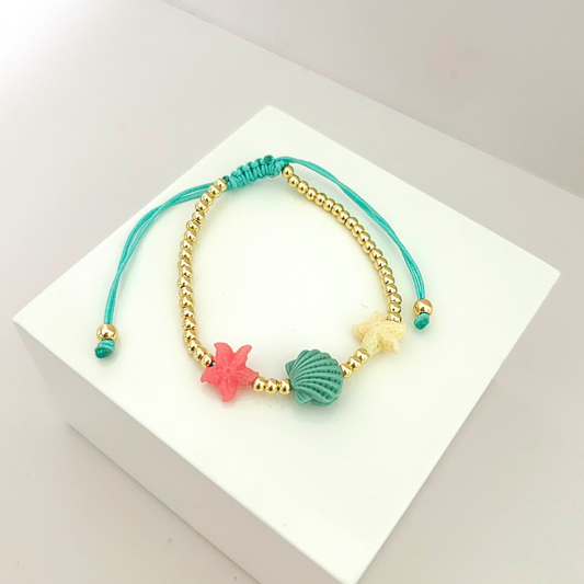 Adjustable beach-inspired bracelet with seashell and starfish charms in pastel colors.