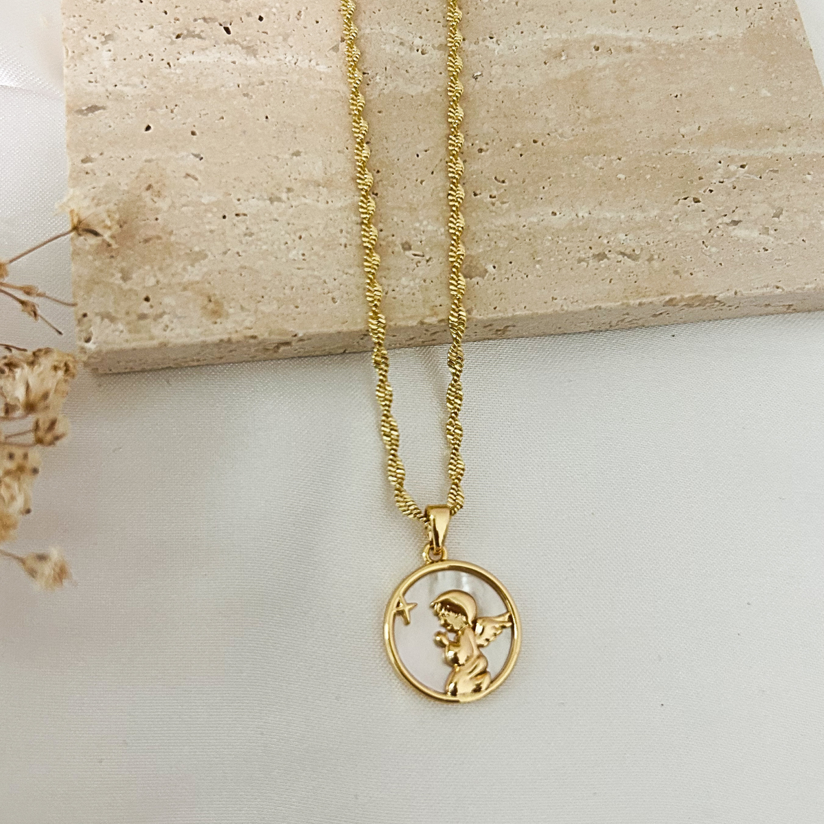 Gold guardian angel pendant necklace with a mother-of-pearl background and textured gold chain, displayed on a neutral minimalist background.