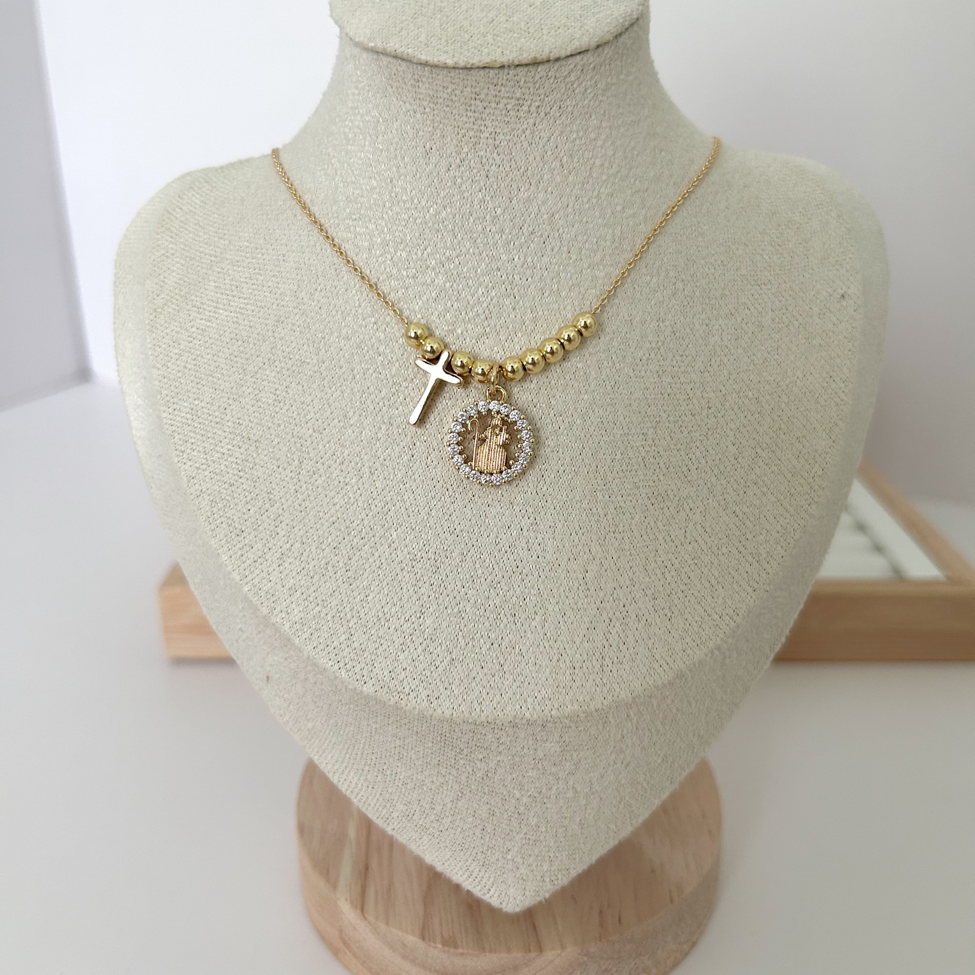Gold beaded necklace with Divina Pastora medallion and cross charm on linen jewelry bust — Citrika