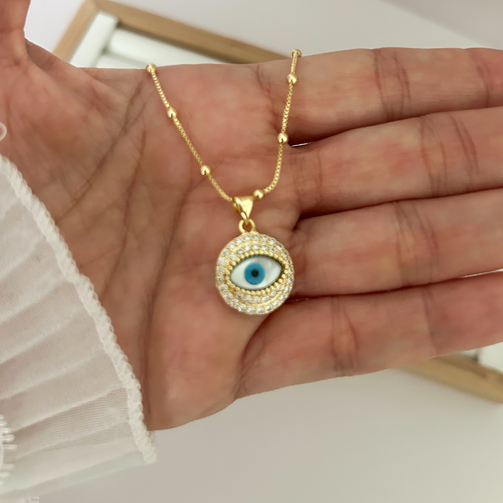 Gold evil eye pendant necklace with blue enamel and zirconia halo on gold chain on white background — Citrika
