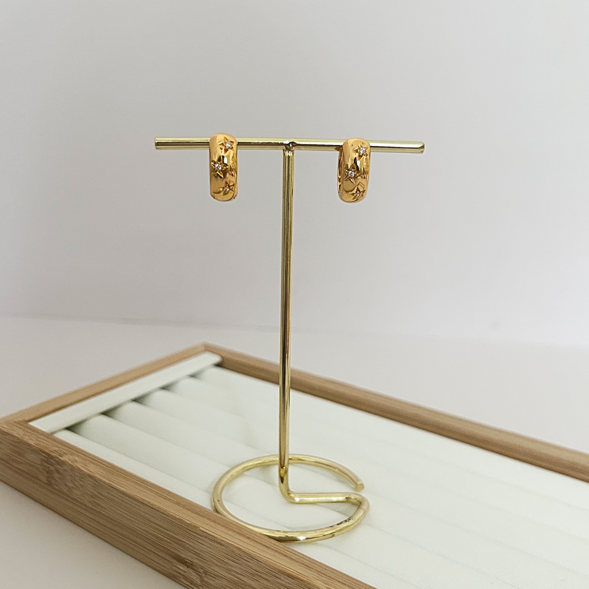 Chunky wide gold huggie earrings with star and crystal detail on jewelry stand