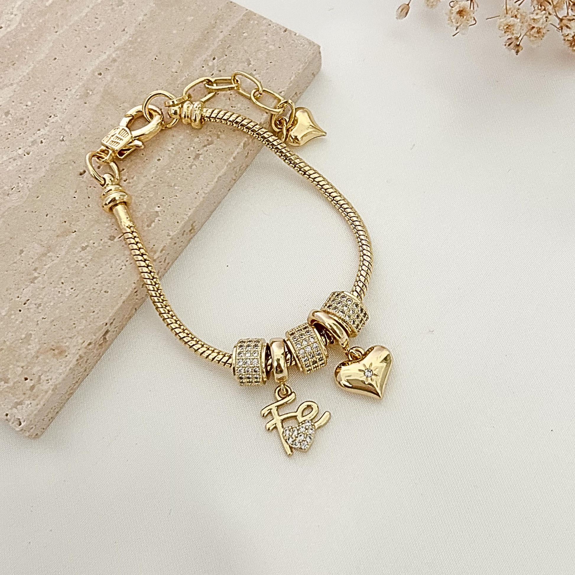 Elegant gold-tone charm bracelet featuring crystal-studded beads, a polished heart charm, and a “Hope” pendant displayed on a neutral background with soft floral accents.