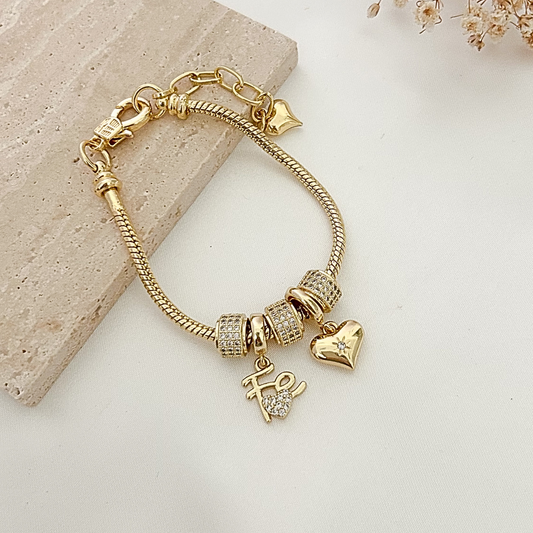 Elegant gold-tone charm bracelet featuring crystal-studded beads, a polished heart charm, and a “Hope” pendant displayed on a neutral background with soft floral accents.