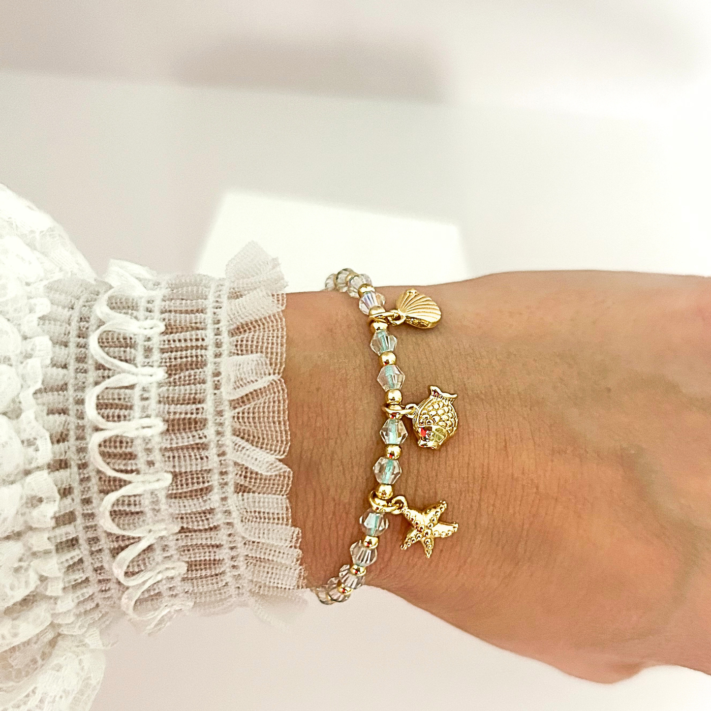 Handmade adjustable bracelet with iridescent crystal beads and gold-tone sea life charms, perfect for summer style.
