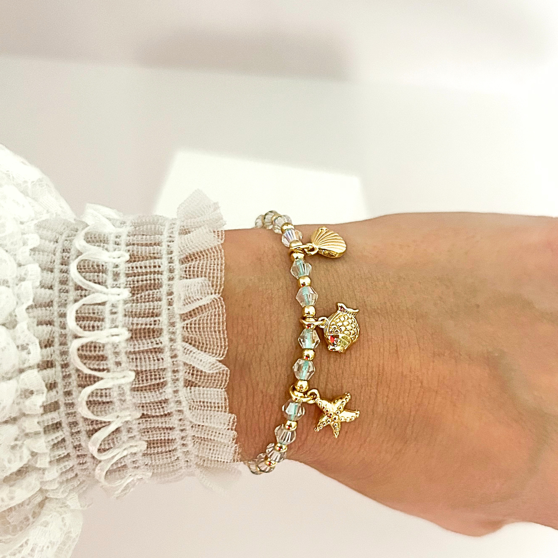 Handmade adjustable bracelet with iridescent crystal beads and gold-tone sea life charms, perfect for summer style.