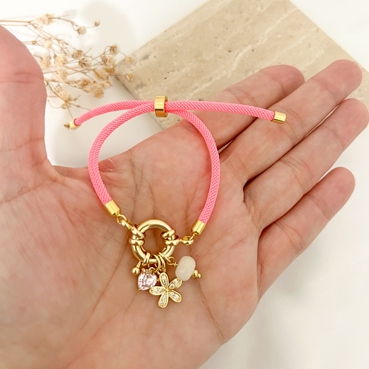 Neon pink cord bracelet with flower and stone charms held in hand