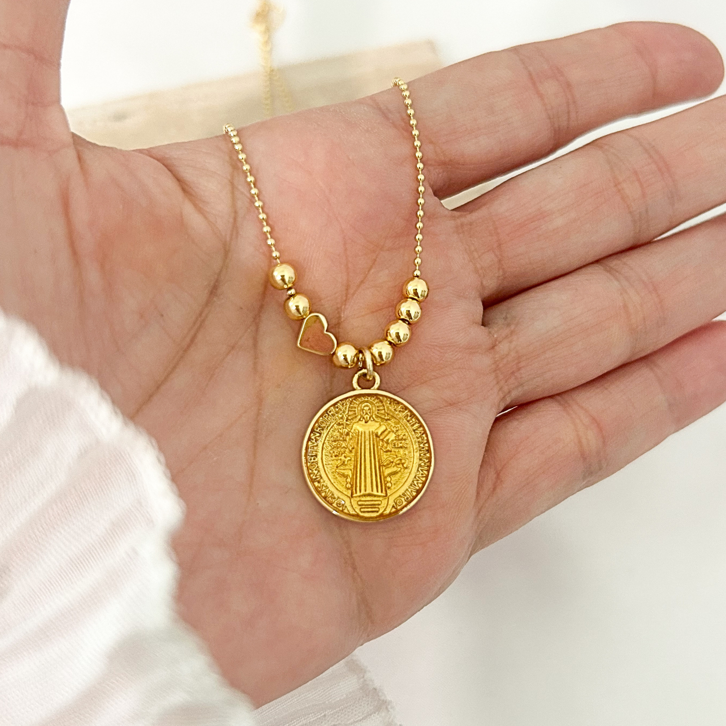 Gold Saint Benedict medallion necklace with polished gold bead accents and a delicate ball chain, displayed on a neutral minimalist background.