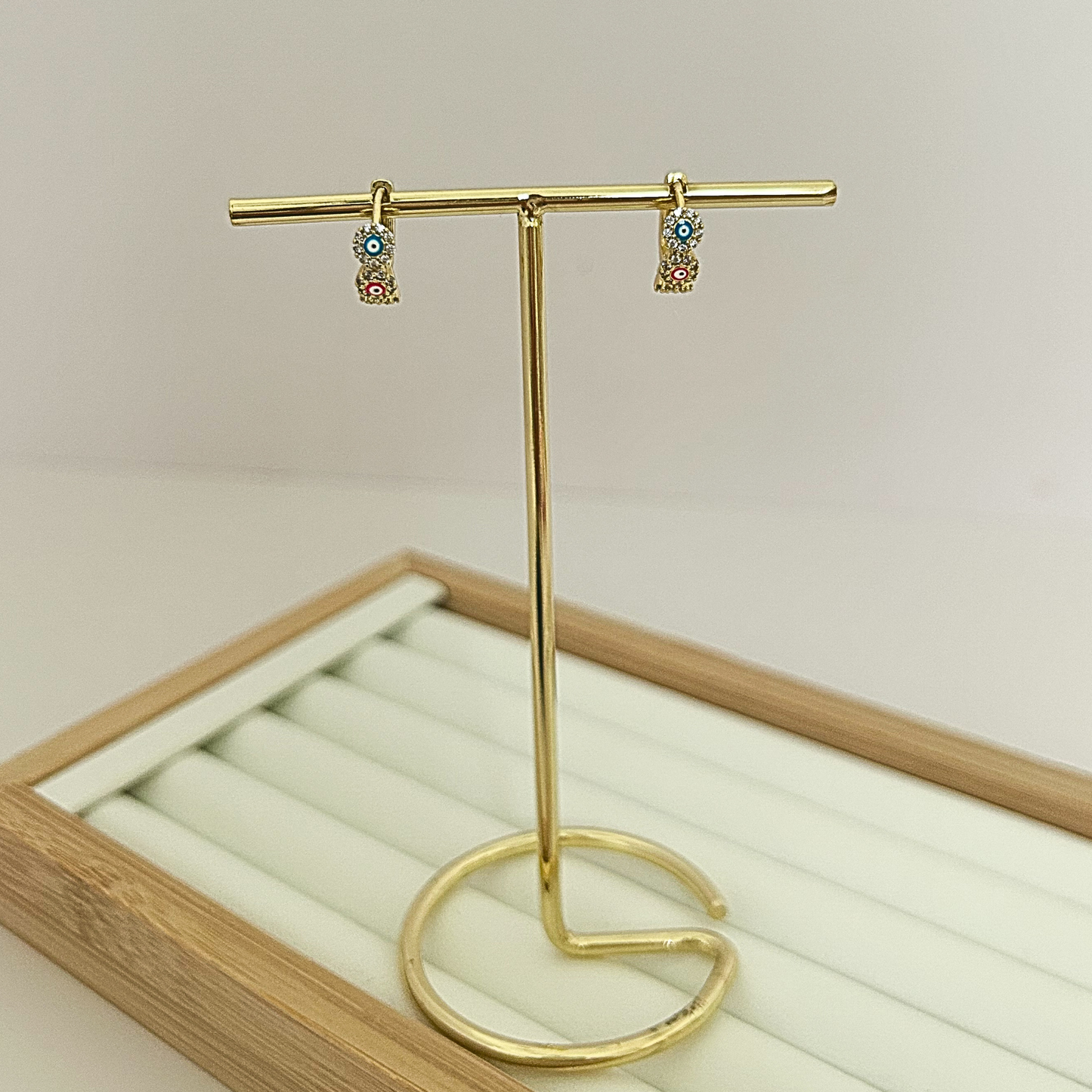 Gold huggie hoop earrings with three multicolor evil eye stones on jewelry stand