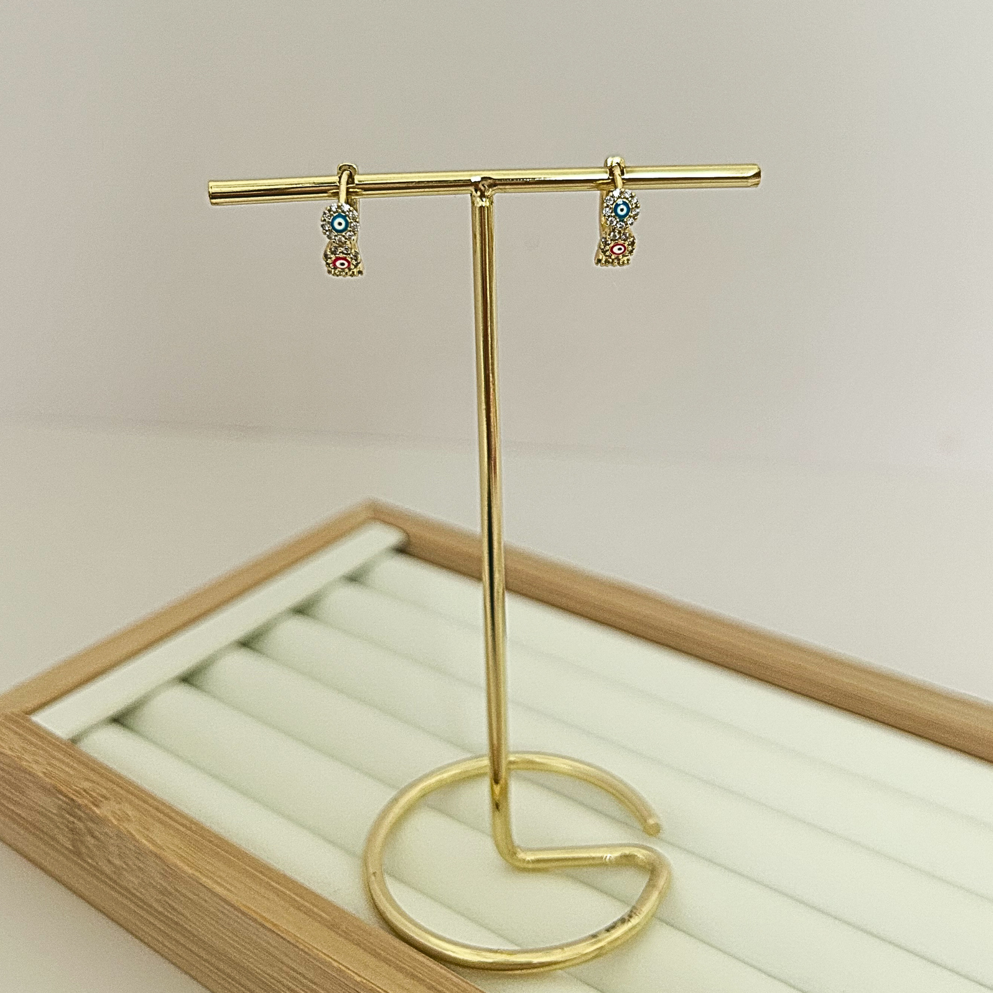 Gold huggie hoop earrings with three multicolor evil eye stones on jewelry stand