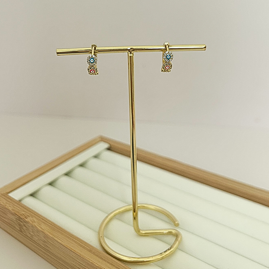 Gold huggie hoop earrings with three multicolor evil eye stones on jewelry stand
