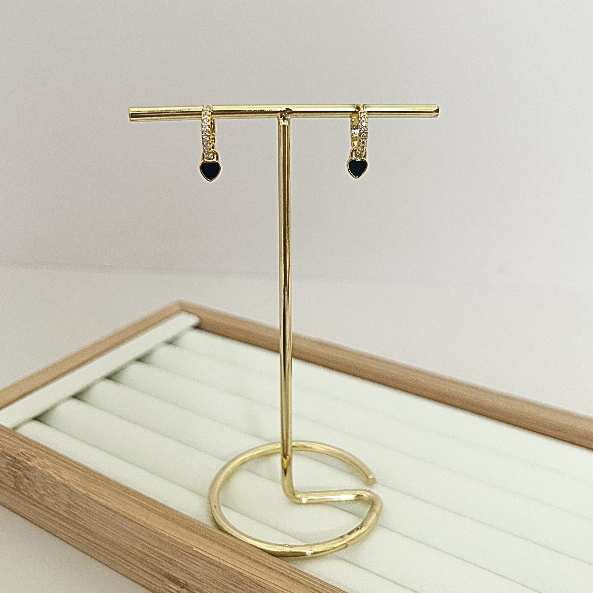 Gold huggie hoop earrings with black enamel heart dangle charm on jewelry stand