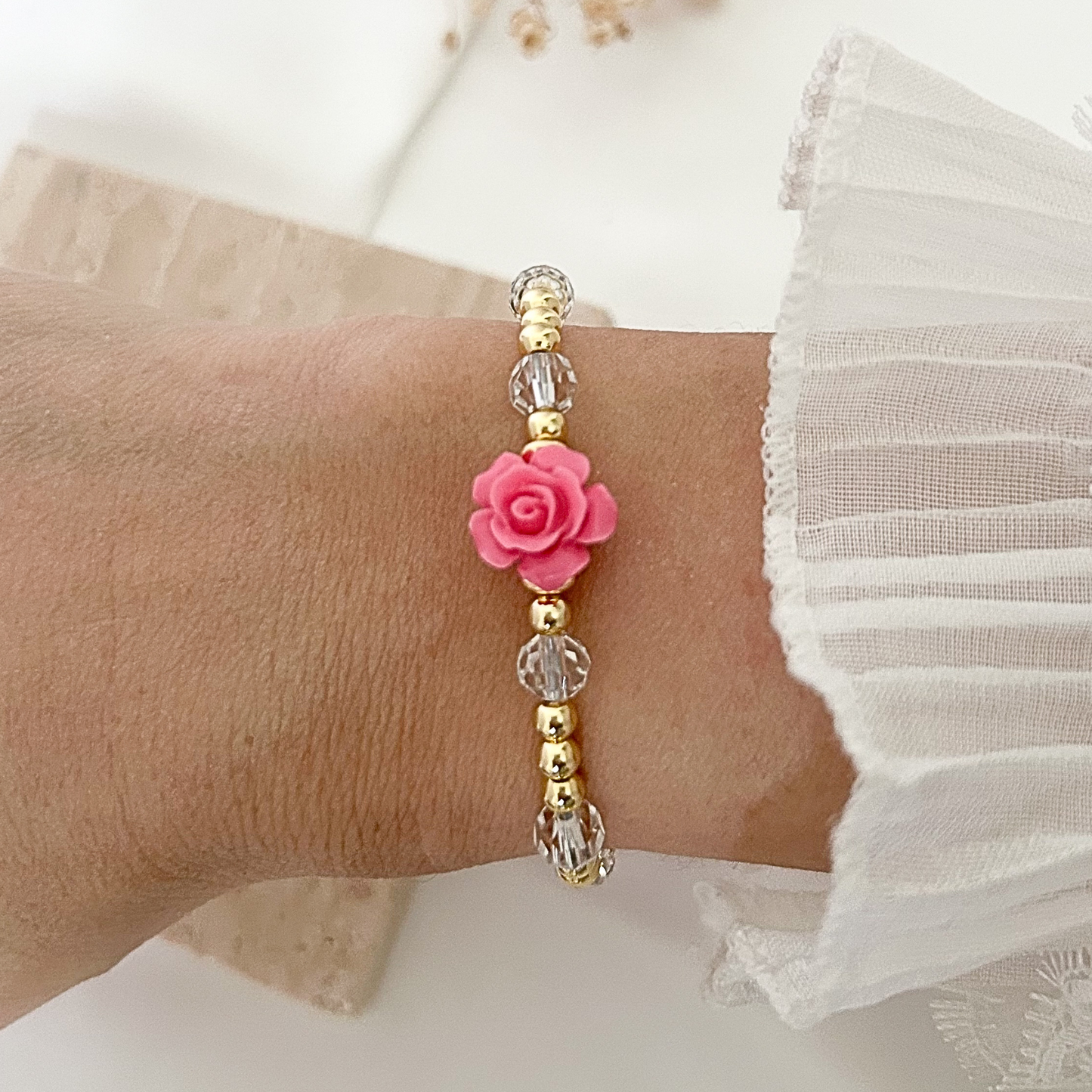 Delicate bracelet with gold-tone beads, clear crystal accents, and a vibrant pink resin rose centerpiece, creating a feminine and elegant look.
