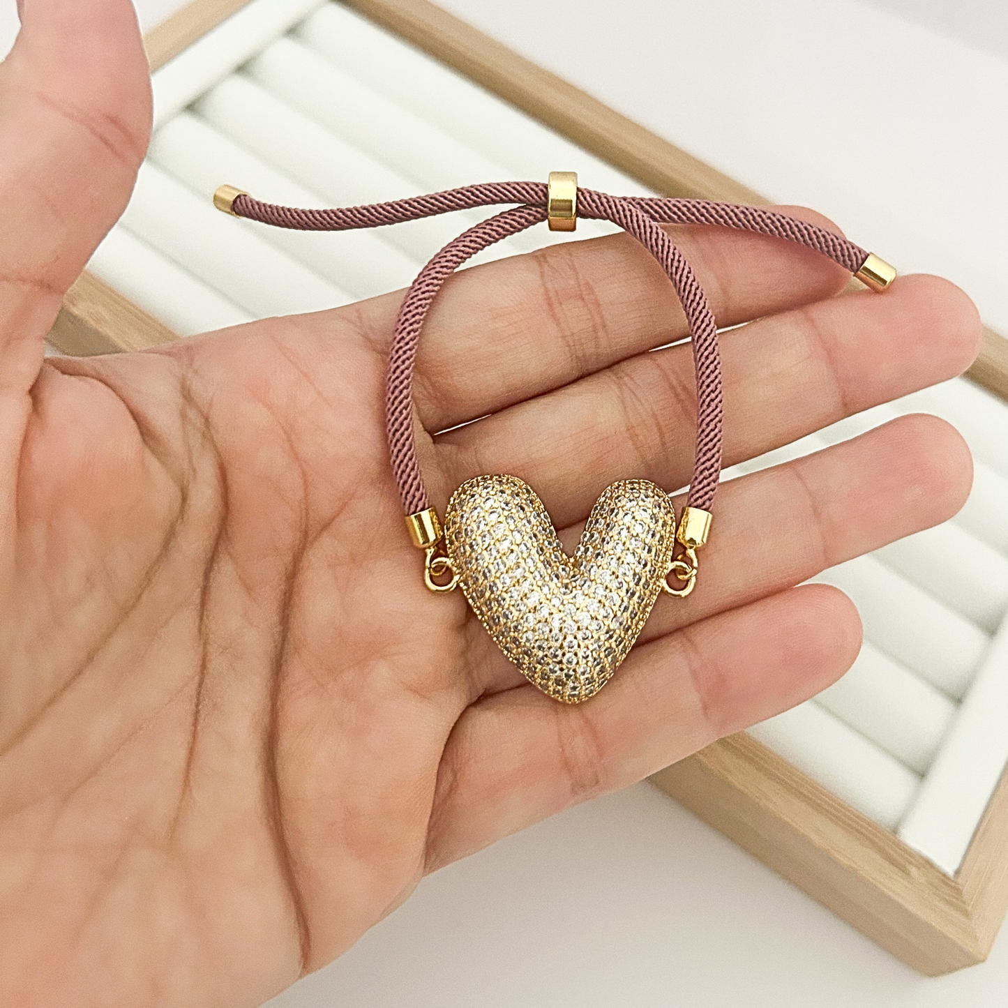 Hand holding adjustable burgundy bracelet with gold crystal heart pendant.