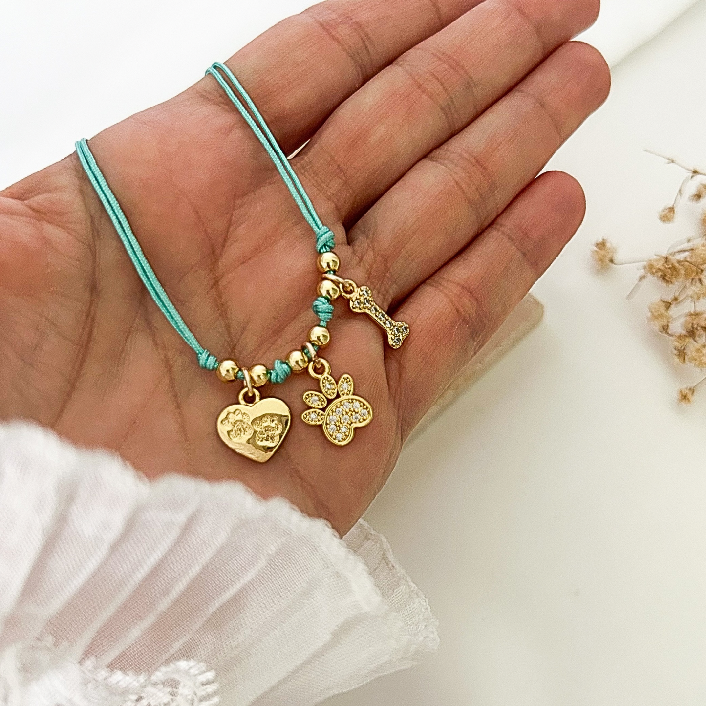 Close-up of a turquoise adjustable bracelet held in hand, showcasing gold pet-themed charms with sparkling details, including a heart with paw prints, a paw charm, and a bone charm, perfect for dog moms and animal lovers.