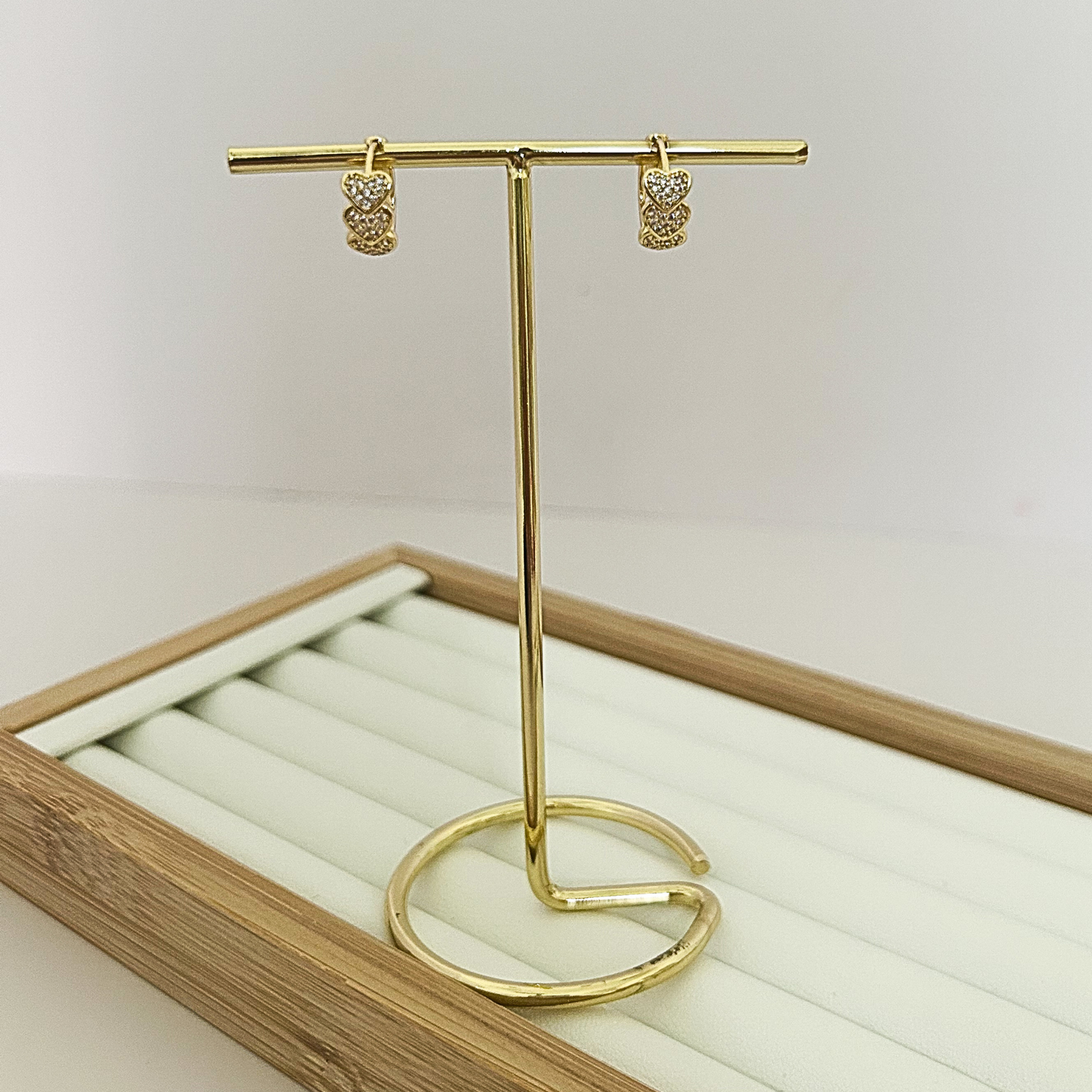 Gold huggie hoop earrings with triple stacked pavé CZ heart charm on jewelry stand