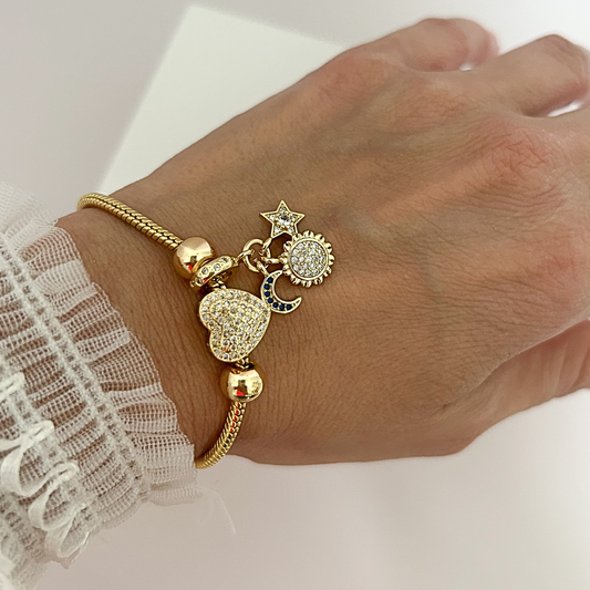 Mujer usando pulsera dorada con charms de corazón, luna, sol y estrella decorados con circonias brillantes.