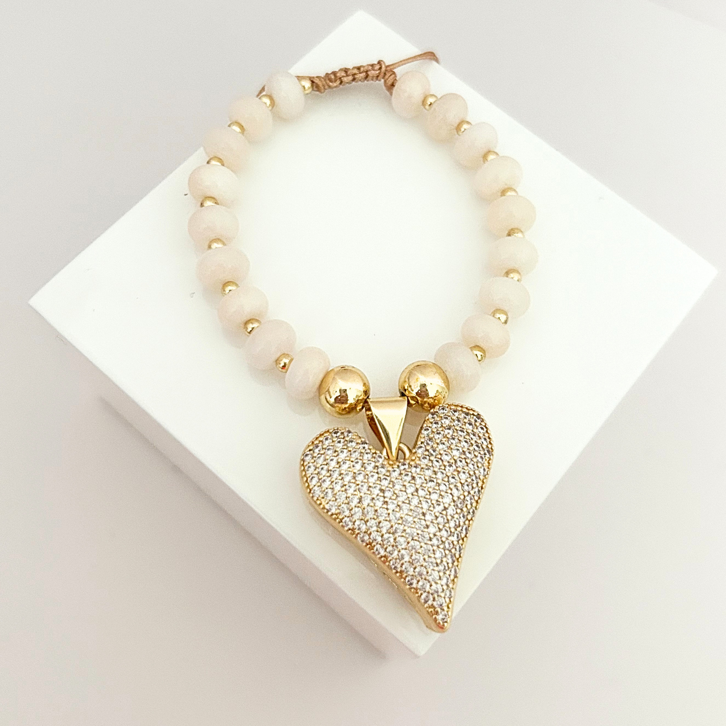 Handmade bracelet featuring ivory beads, gold-tone accents, and a shimmering crystal heart charm with adjustable closure.