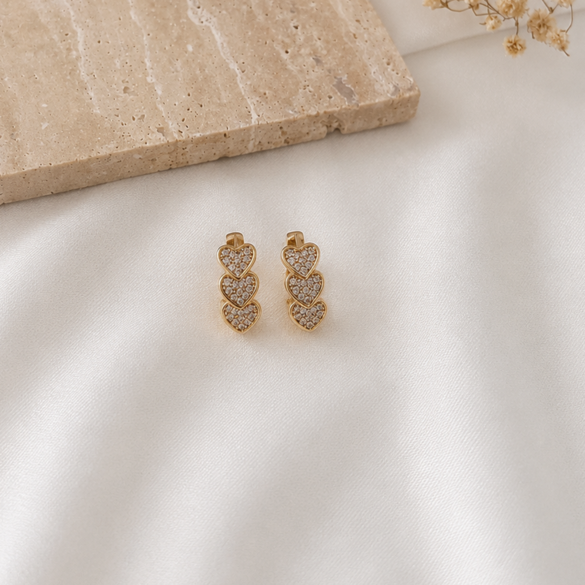 Pair of gold-tone earrings featuring three vertically stacked pavé heart charms adorned with sparkling cubic zirconia. Elegant and romantic statement earrings with a polished gold finish, perfect for everyday wear, date nights, special occasions, or gifting.