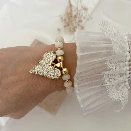 Elegant handmade bracelet featuring natural-look ivory beads and a pavé heart pendant in gold-tone finish, worn on the wrist.
