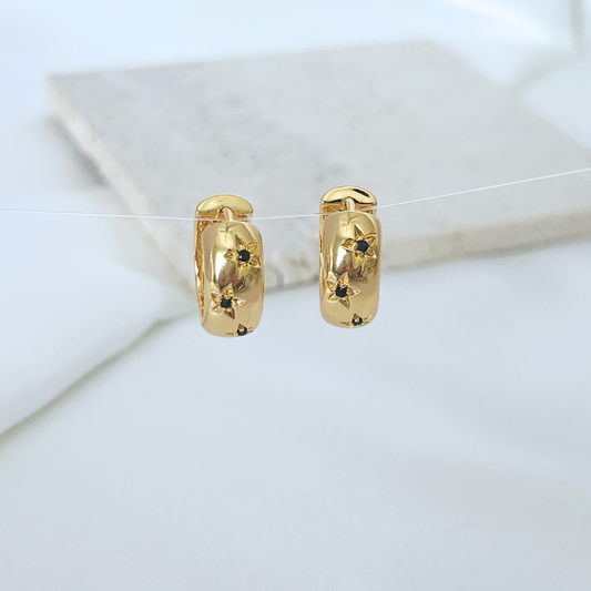 Gold hoop earrings with black stones on a white surface