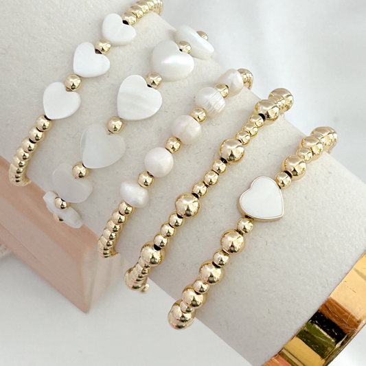 Two gold and white beaded bracelets on a white surface