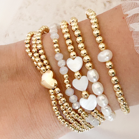 Gold and pearl beaded bracelets on a wrist against a neutral background