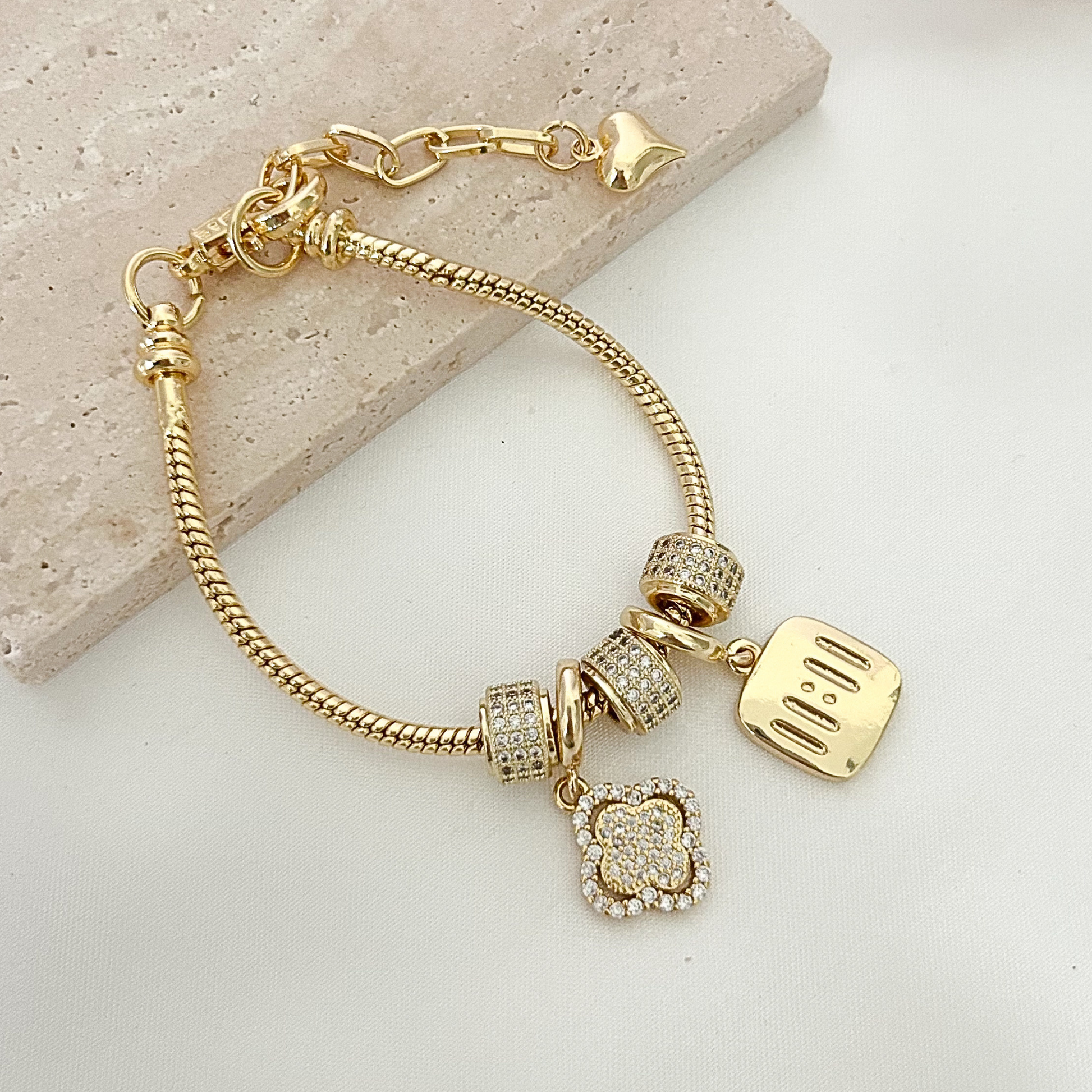 Elegant gold bracelet with crystal-studded charms and a dangling “mom” pendant displayed on a neutral stone surface with soft dried florals, creating a timeless gift presentation.