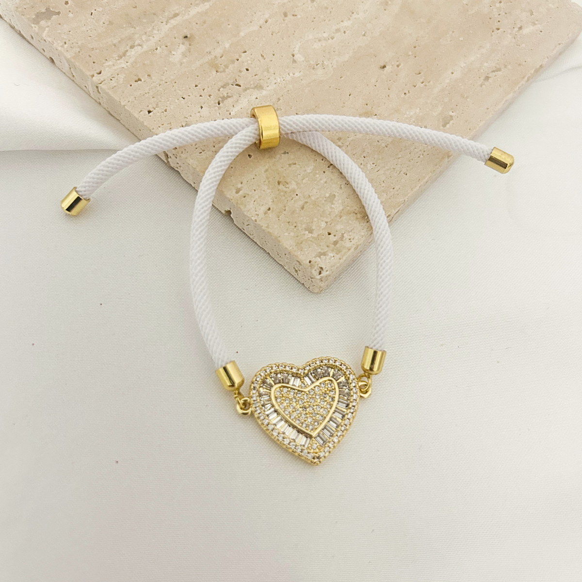 White cord bracelet with pavé baguette heart charm on a stone tray