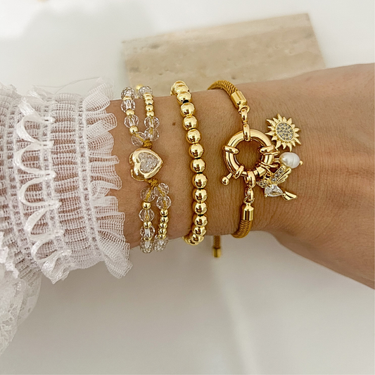 Stacked gold bracelet set with crystal heart, gold bead, and sun hummingbird charm bracelets